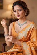 Woman in an orange saree with intricate patterns, sitting indoors.