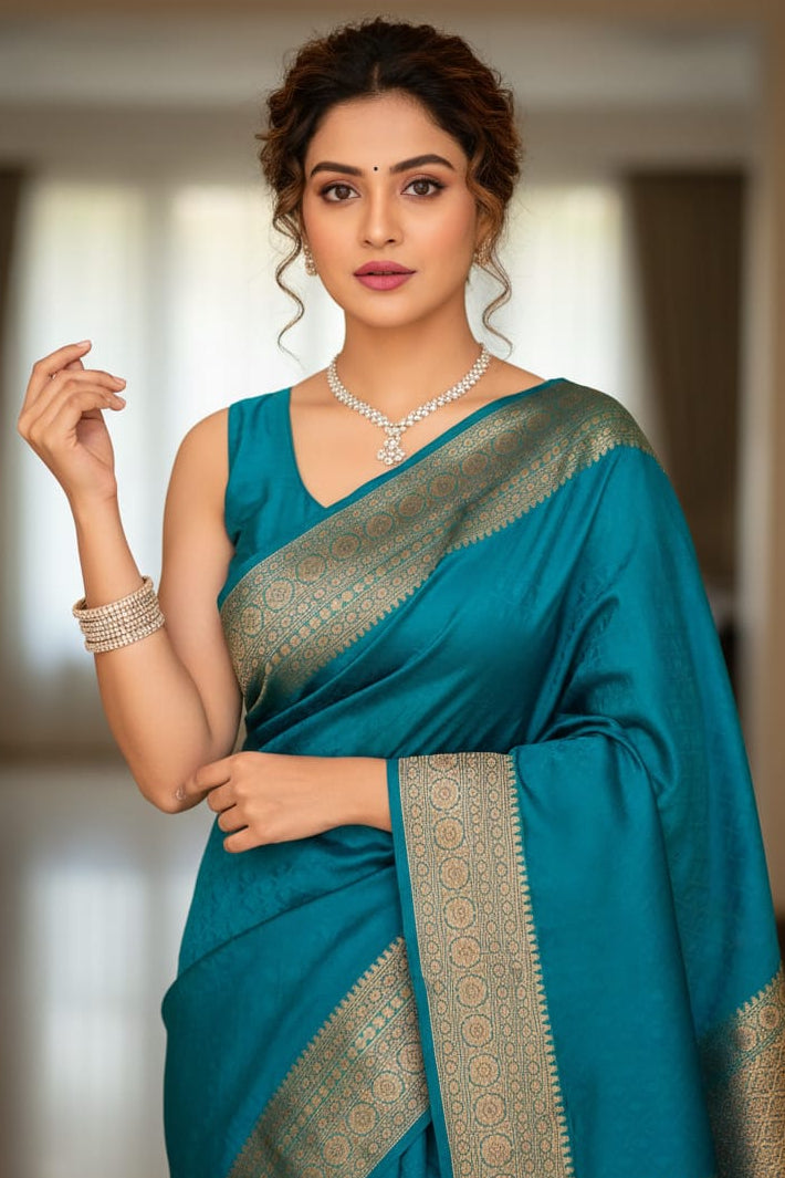 Woman wearing a teal saree with gold border indoors