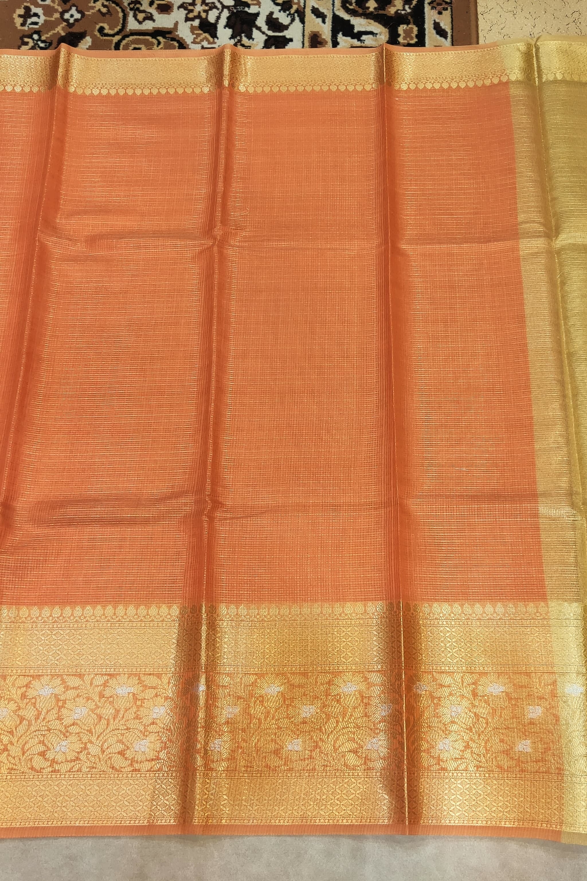 Orange saree with a gold border on a neutral background