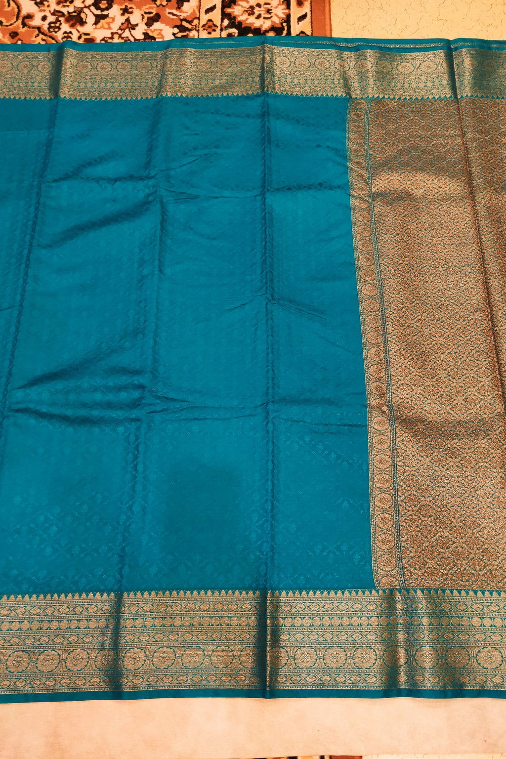 Teal saree with a gold border on a beige background