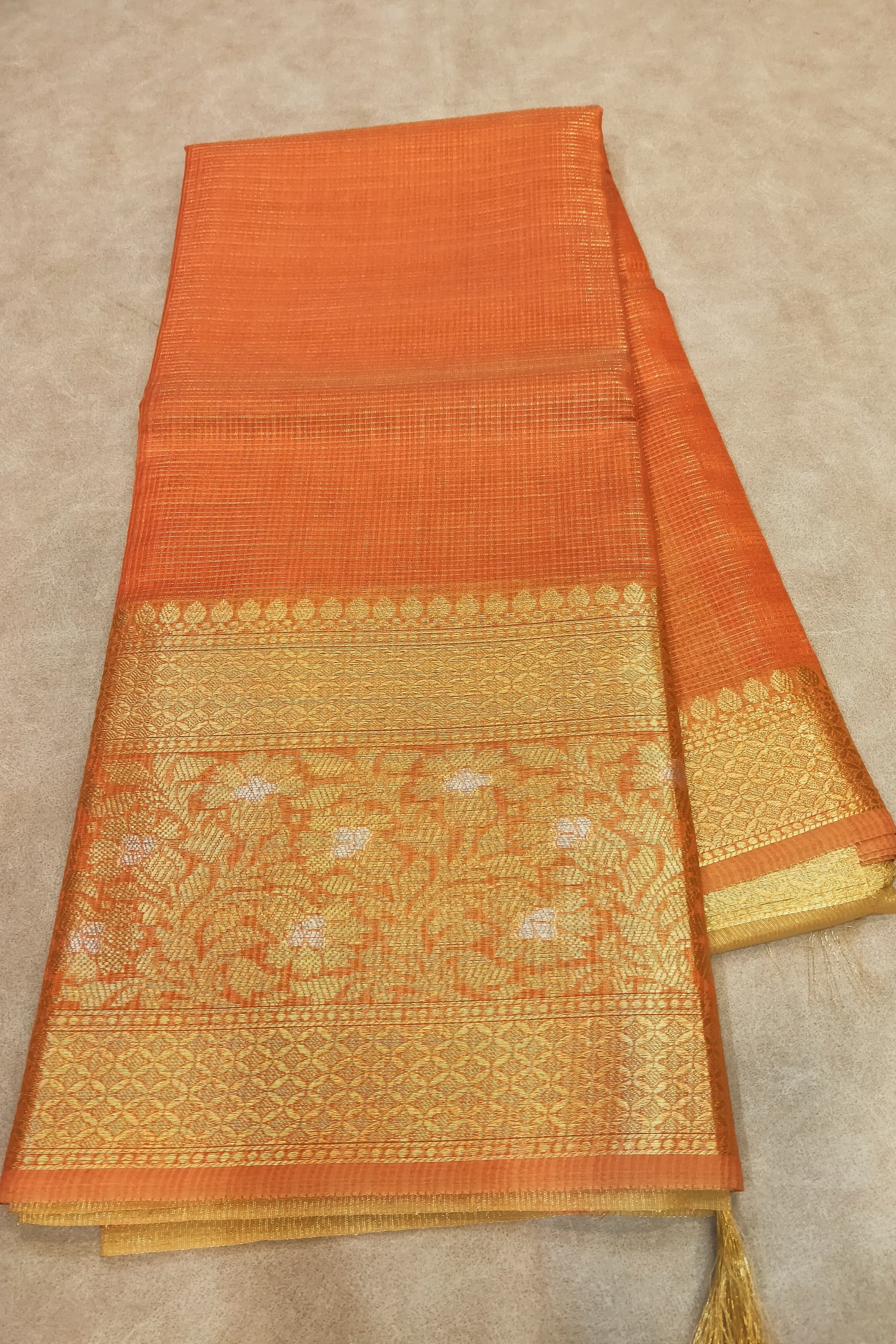 Orange and gold saree with intricate patterns on a beige background