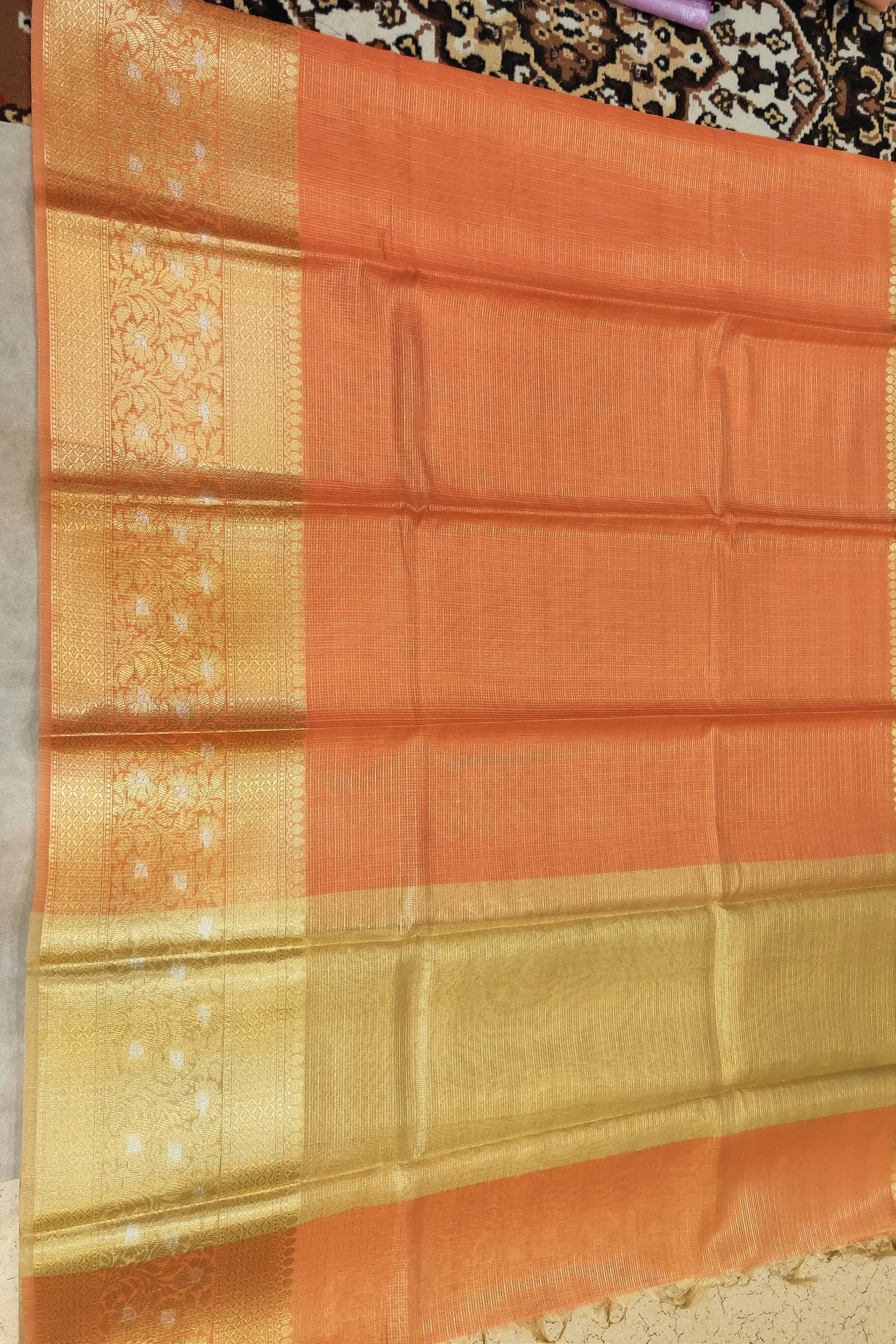 Orange and gold traditional fabric with intricate patterns on a neutral background