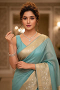 Woman in a light blue saree with a blurred indoor background