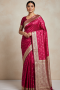 Woman wearing a pink saree with gold border against a beige background