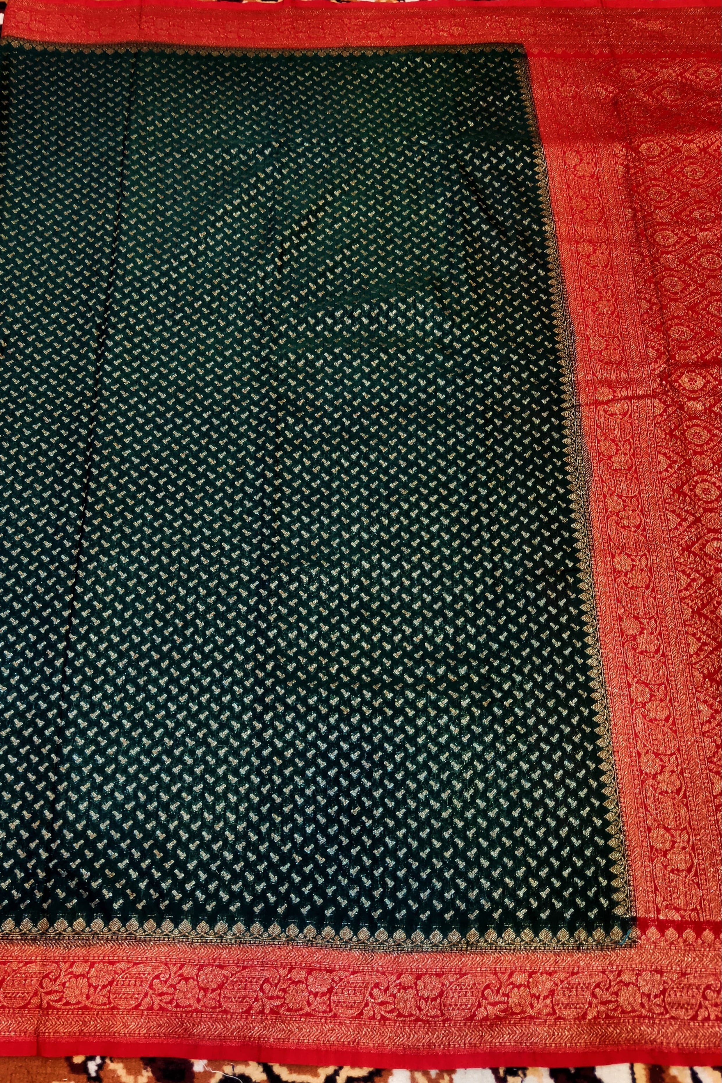 Dark green saree with red border on a patterned fabric background