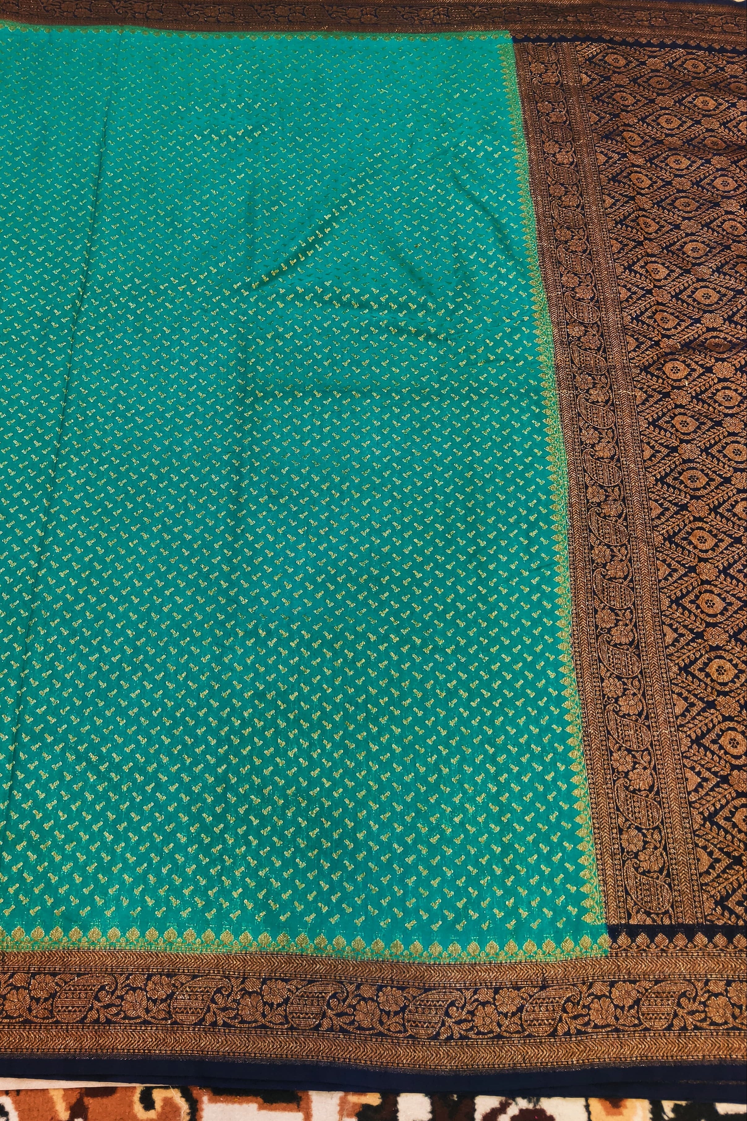 Green fabric with brown border on a patterned carpet