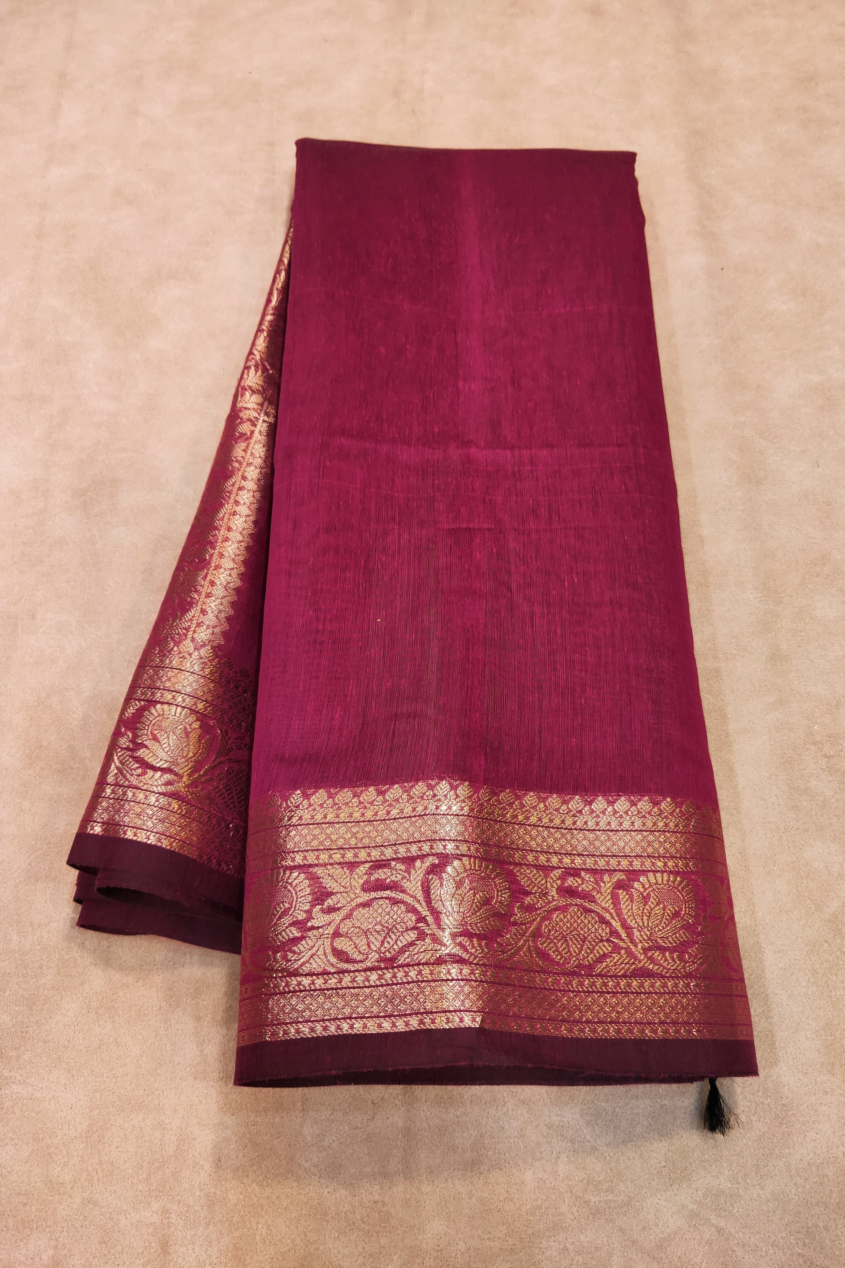 Maroon saree with gold border on a beige background