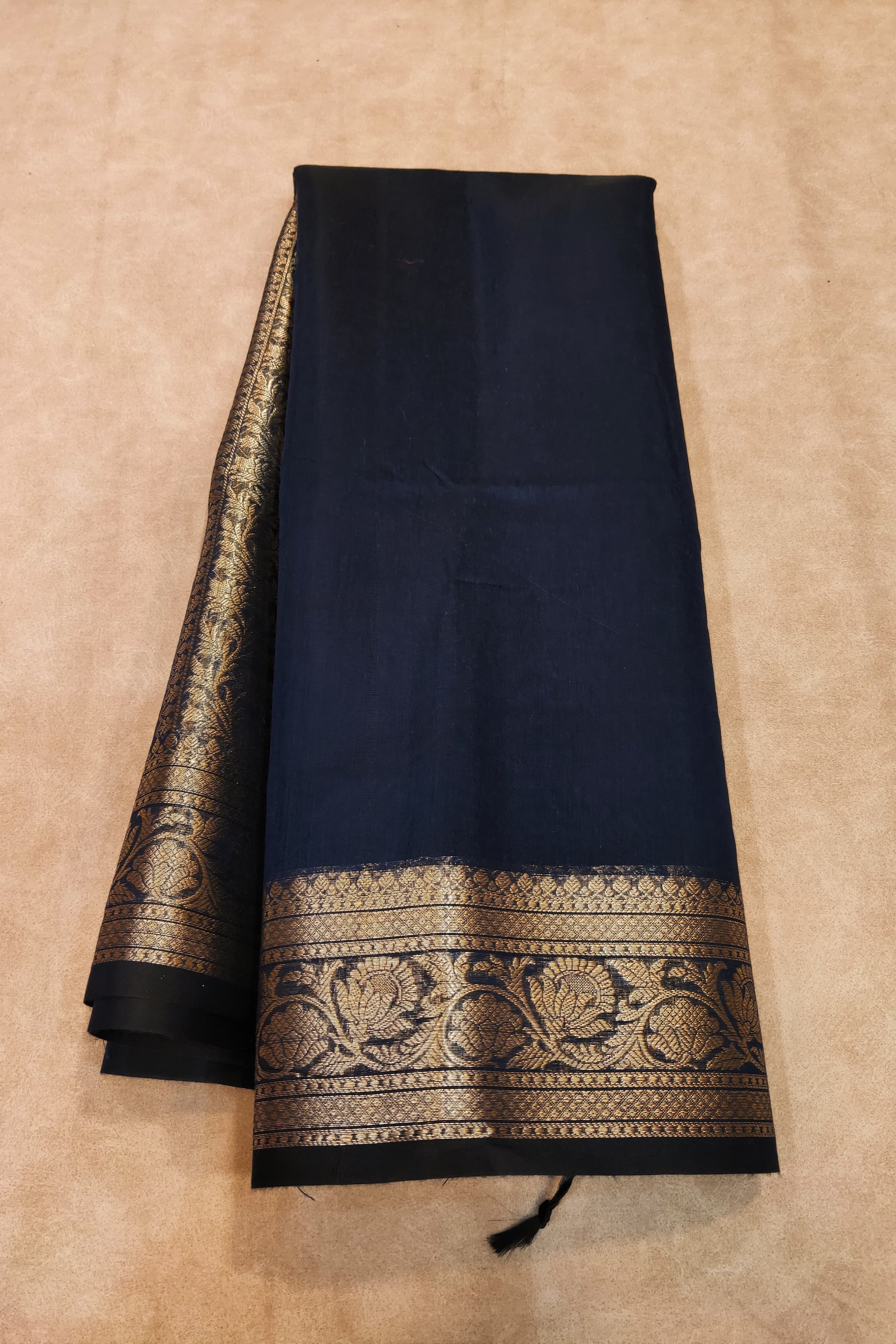 Black saree with gold border on a beige background