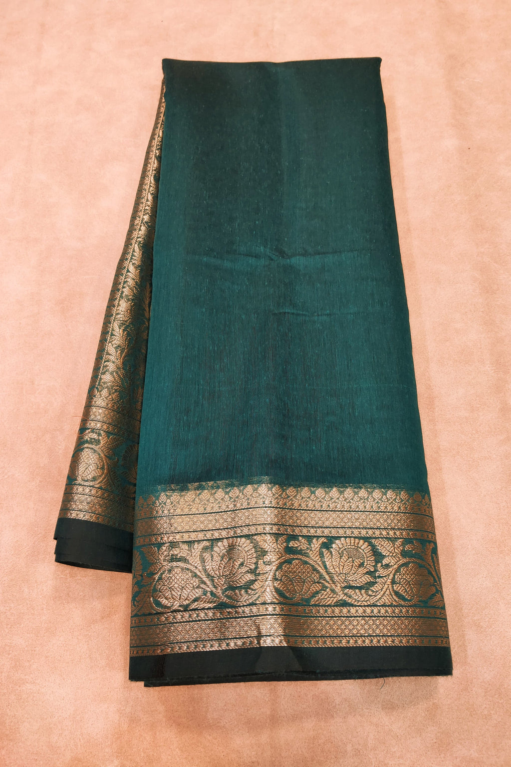 Teal saree with black and gold border on a beige background