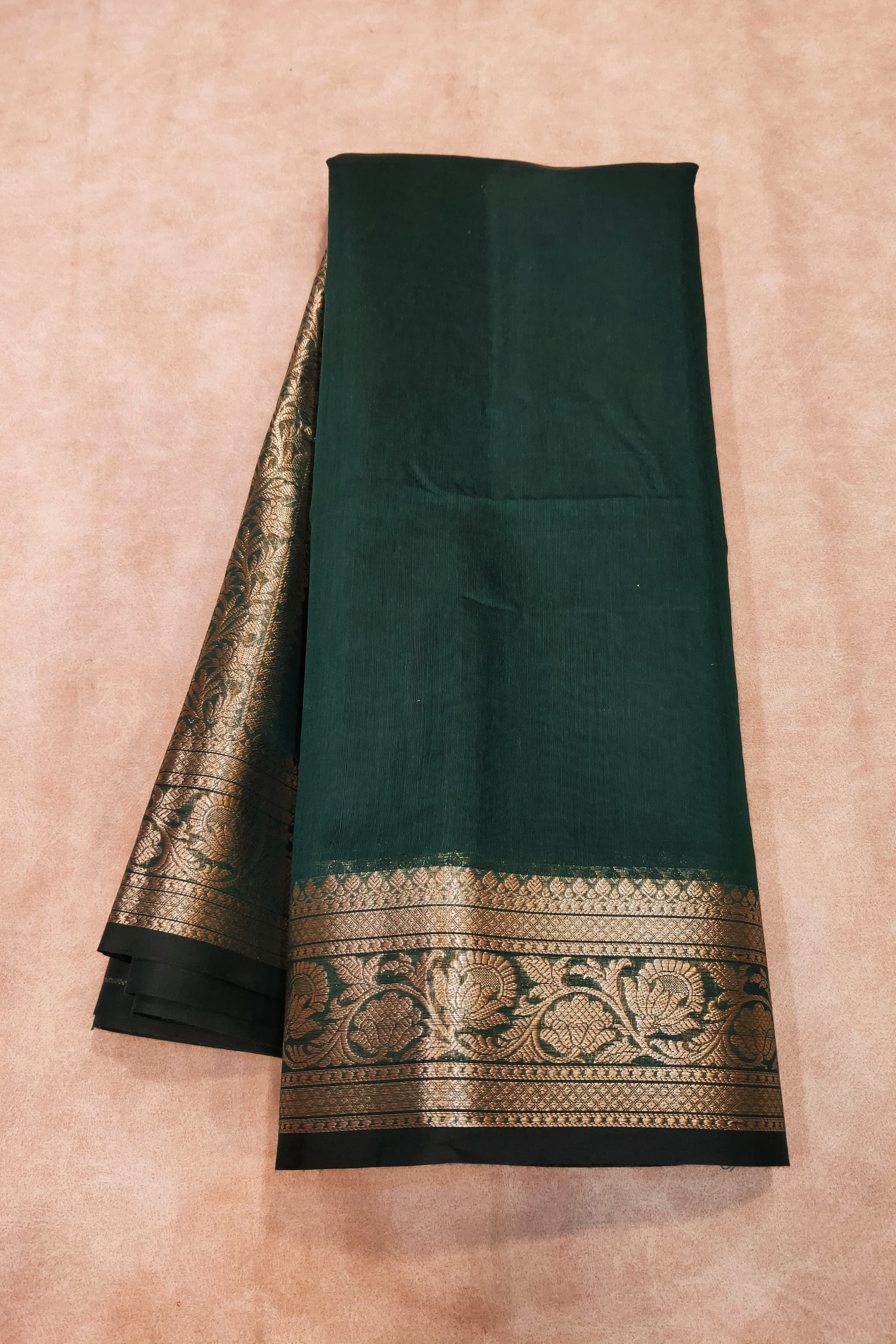 Dark green saree with gold border on a beige background