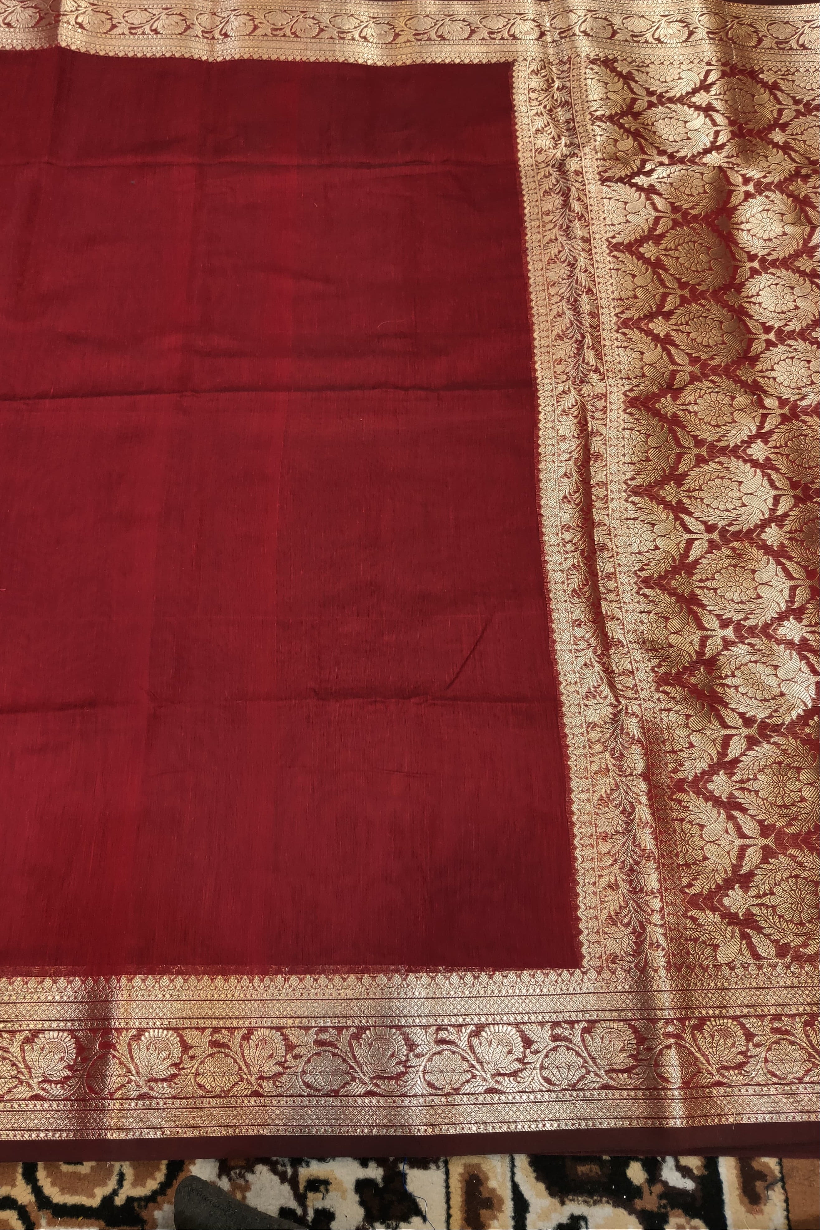 Red fabric with intricate gold border on a patterned surface