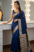 Woman in a blue saree with gold patterns standing in front of a mirror.