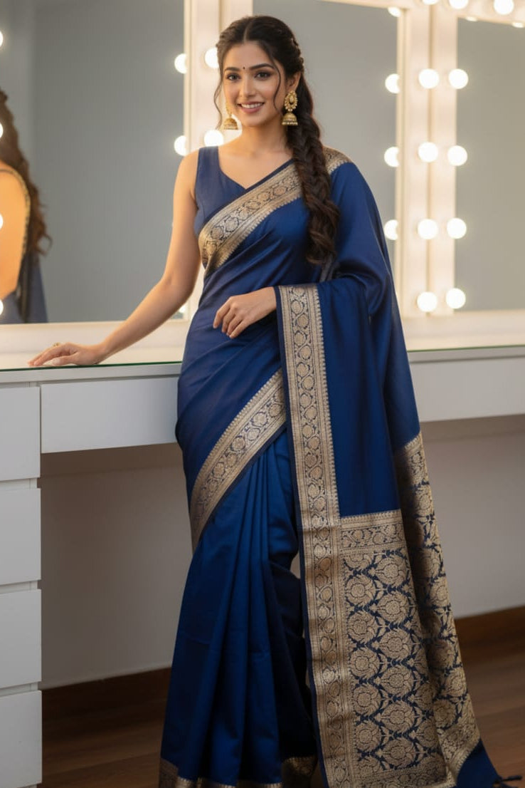 Woman in a blue saree with gold patterns standing in front of a mirror.