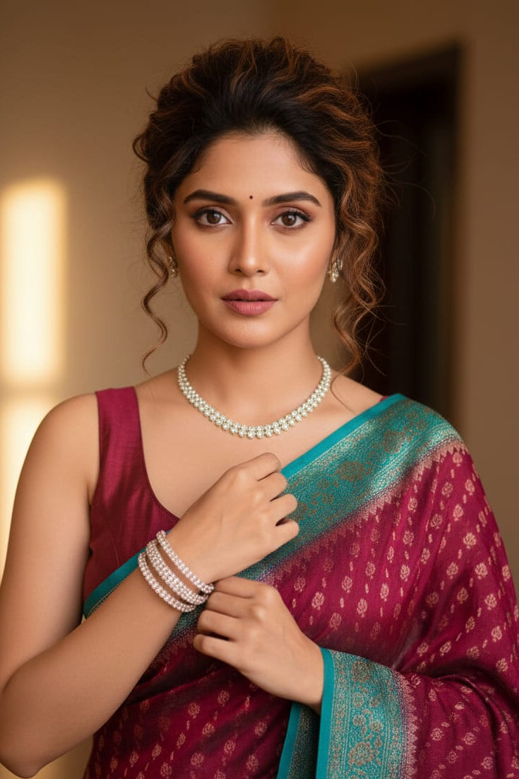 Woman in a maroon saree with a blue border, wearing jewelry, against a warm-toned background.