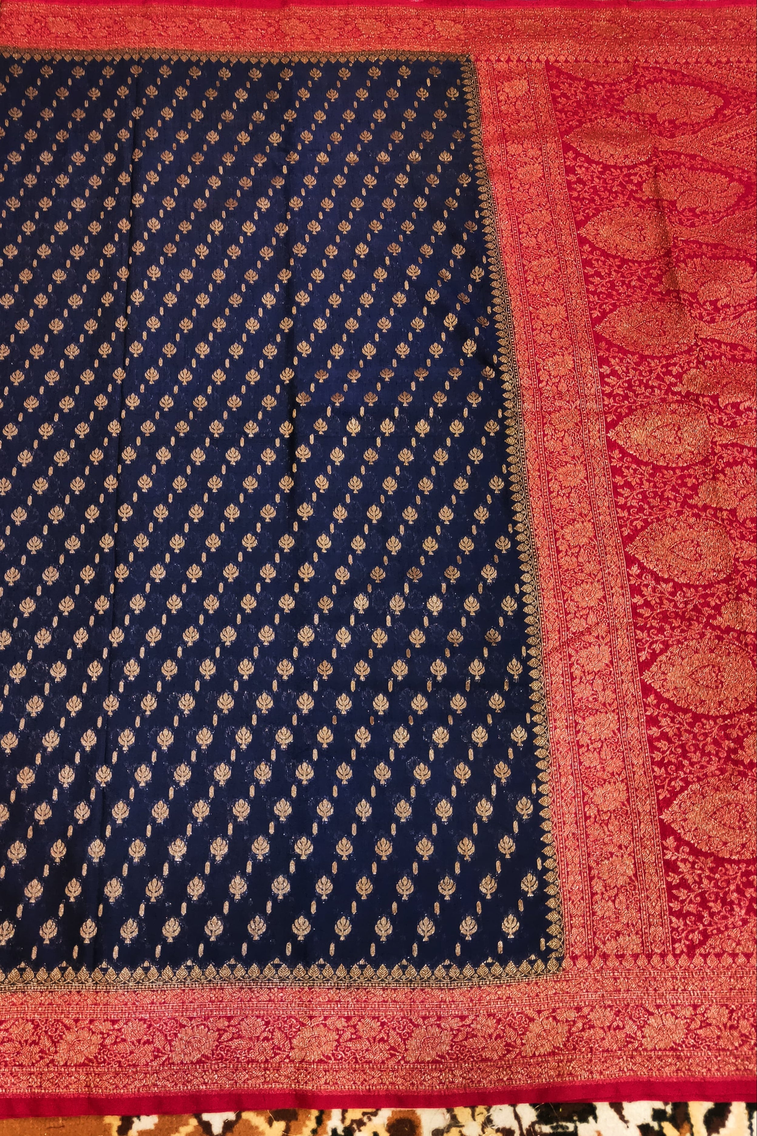 Navy blue fabric with gold patterns on a red border against a patterned background