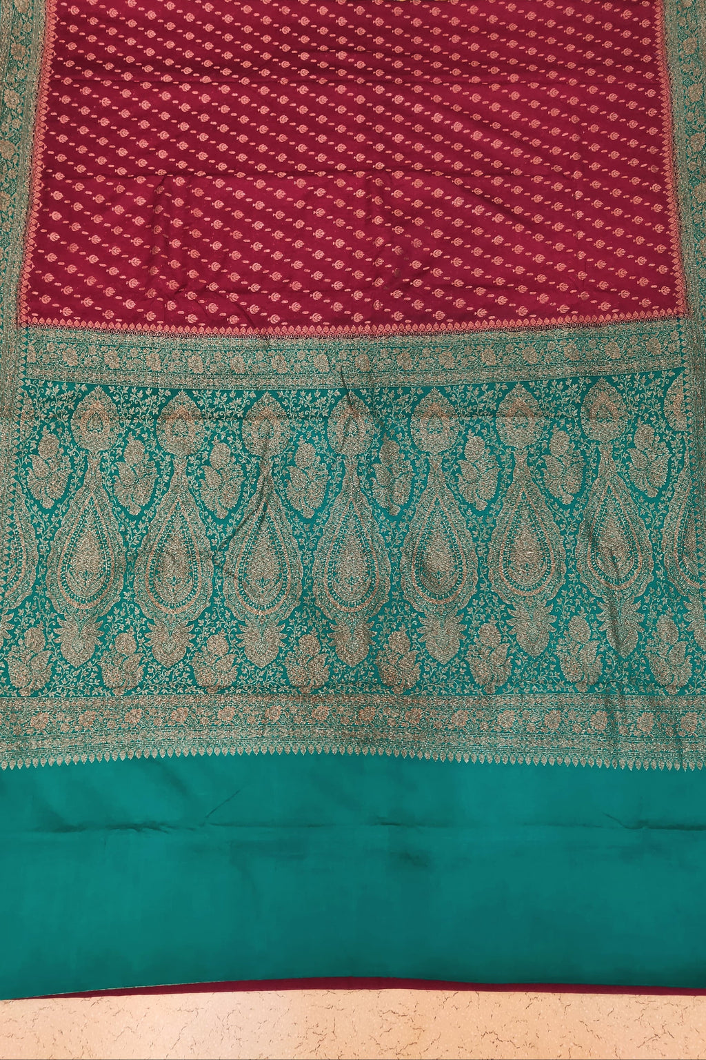 Traditional maroon and teal fabric with intricate patterns on a patterned background