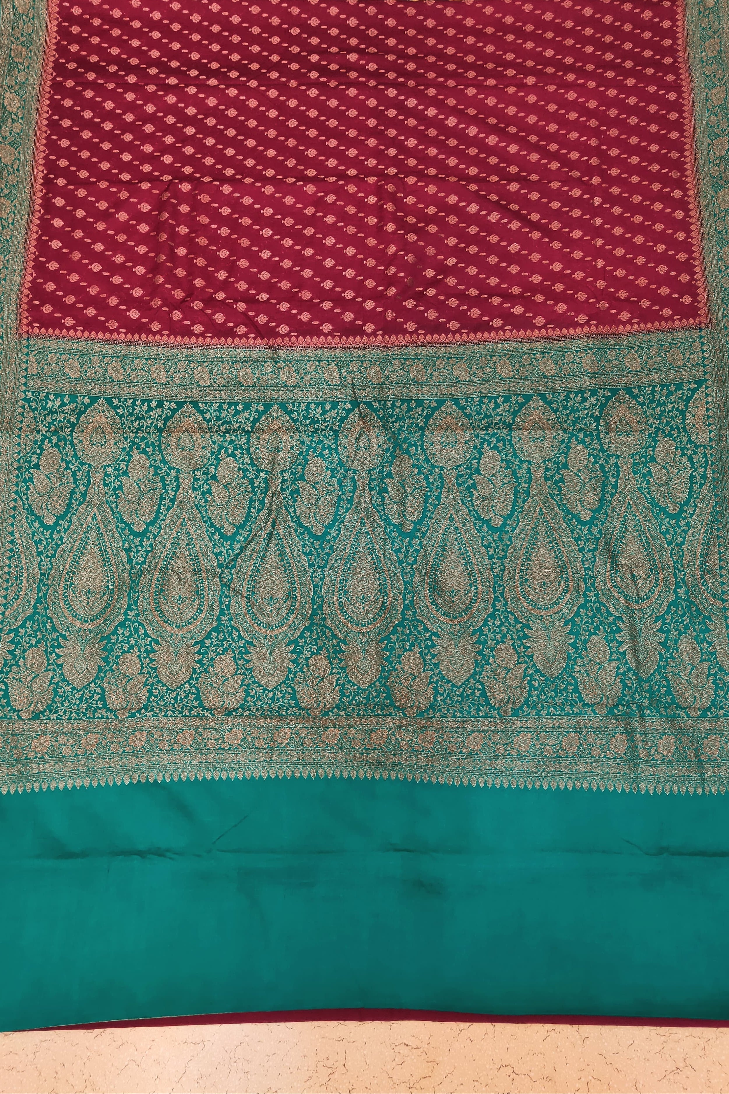 Traditional maroon and teal fabric with intricate patterns on a patterned background