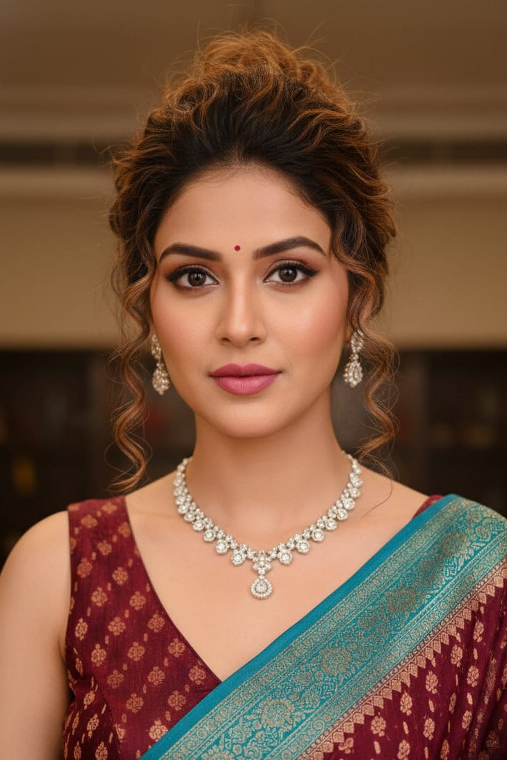 Woman wearing a maroon saree with a blue border and diamond necklace indoors.