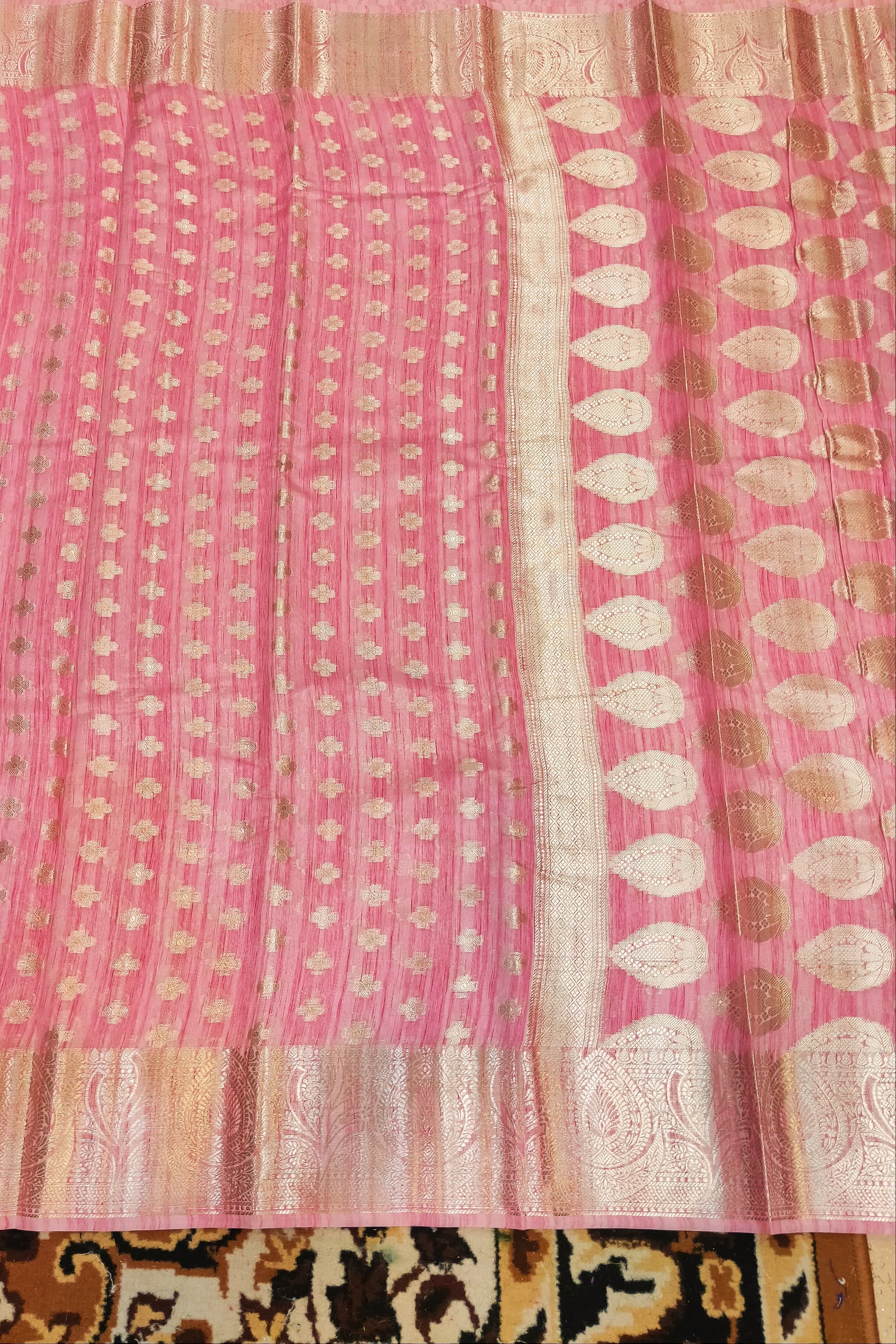 Pink fabric with white and gold patterns on a textured surface