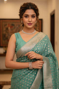 Woman in a teal saree with silver border indoors