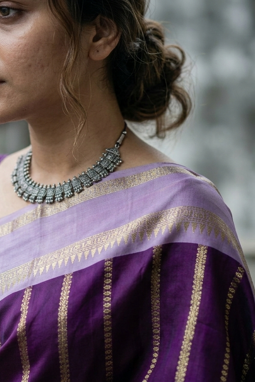 Woman wearing a purple saree with gold patterns, standing outdoors.