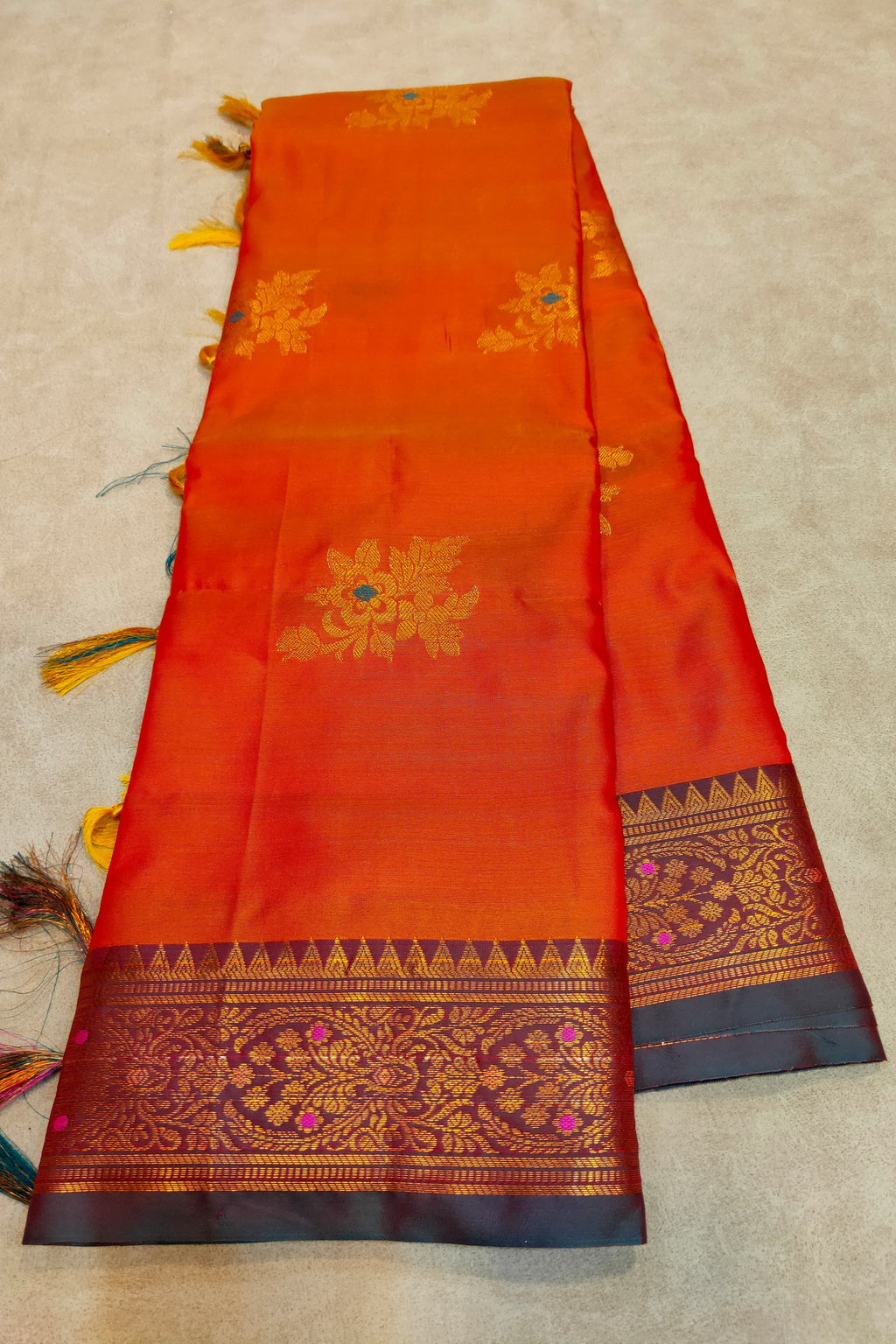 Orange saree with gold and blue patterns on a beige background