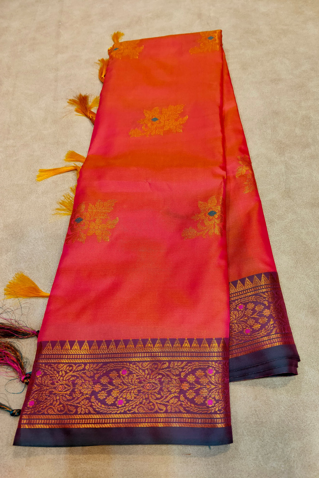 Red and orange saree with gold and blue patterns on a beige background