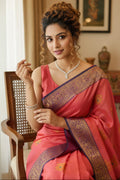 Woman in a pink saree with intricate designs sitting indoors.